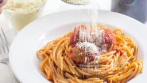 Sprinkling Parmesan cheese over spaghetti and meatballs.