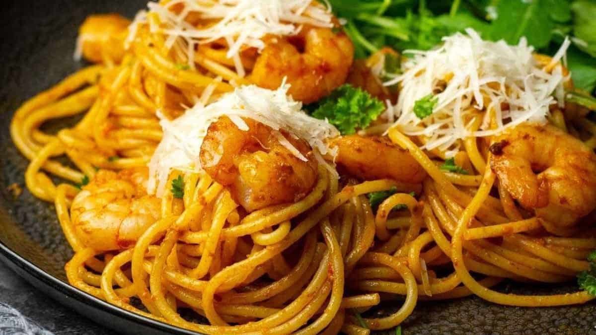 Red pesto pasta with prawns on a black plate.