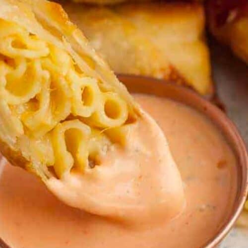 Mac and cheese egg roll being dipped in sauce.