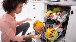 A woman looking at a dishwasher with dirty dishes.