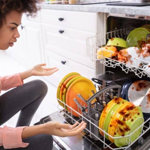A woman looking at a dishwasher with dirty dishes.