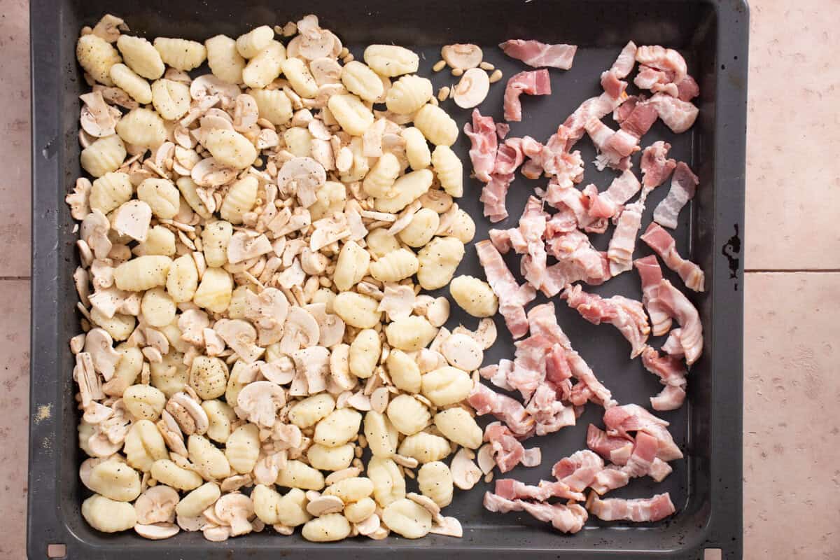 A sheet pan with gnocchi on one side and bacon on the other side, before cooking.