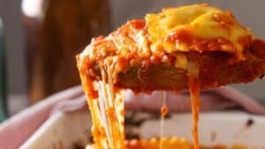 A spoonful of lazy lasagna being lifted out of a baking dish with an amazing cheese pull.