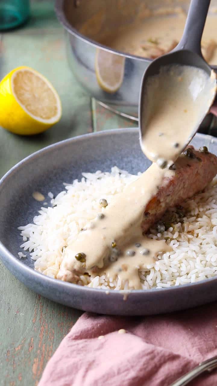 Pouring sauce over salmon piccata and rice.