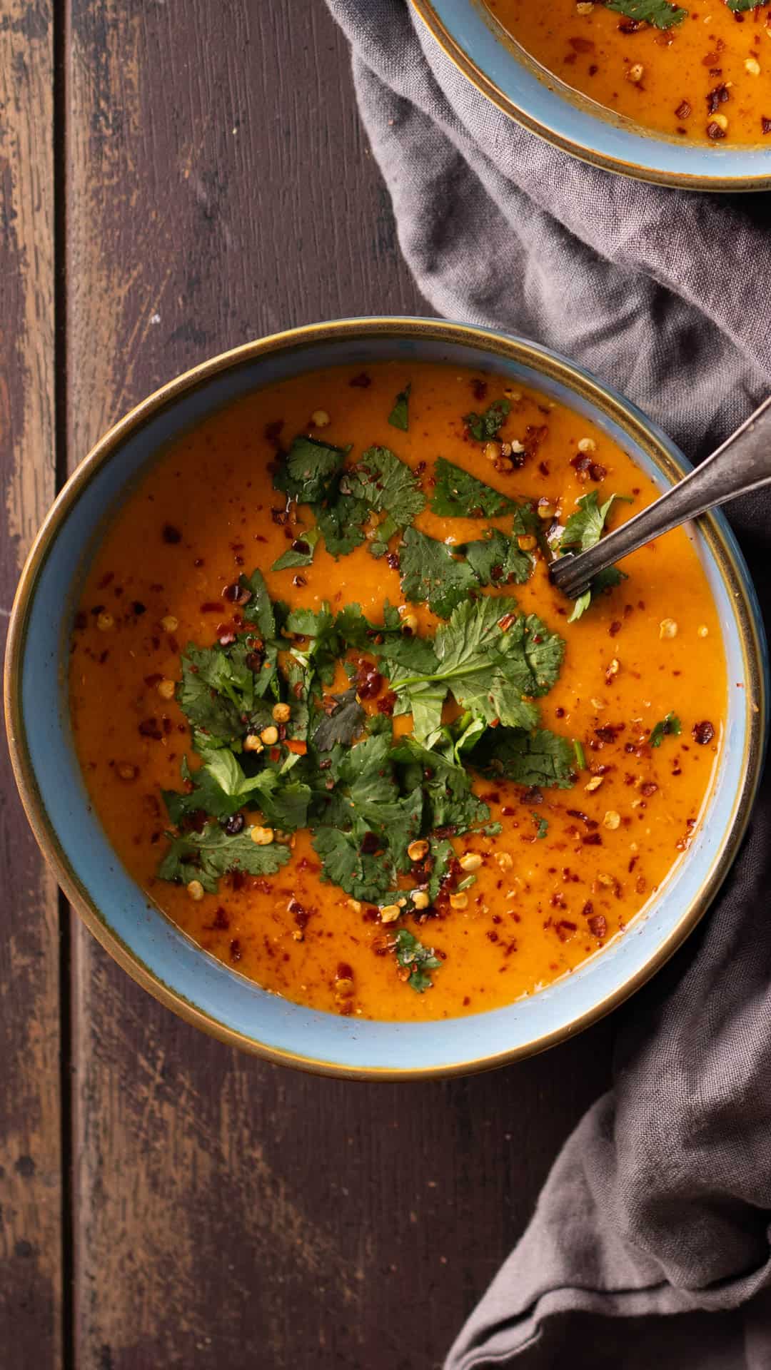 A blue bowl of creamy coconut lentil soup topped with chili flakes and cilantro.