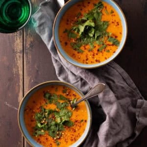 A blue bowl of creamy coconut lentil soup topped with chili flakes and cilantro.