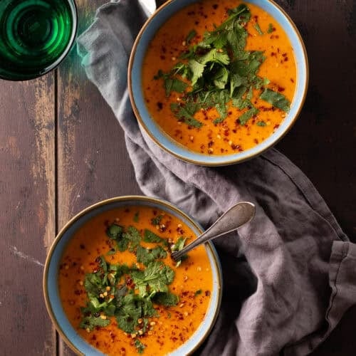 A blue bowl of creamy coconut lentil soup topped with chili flakes and cilantro.