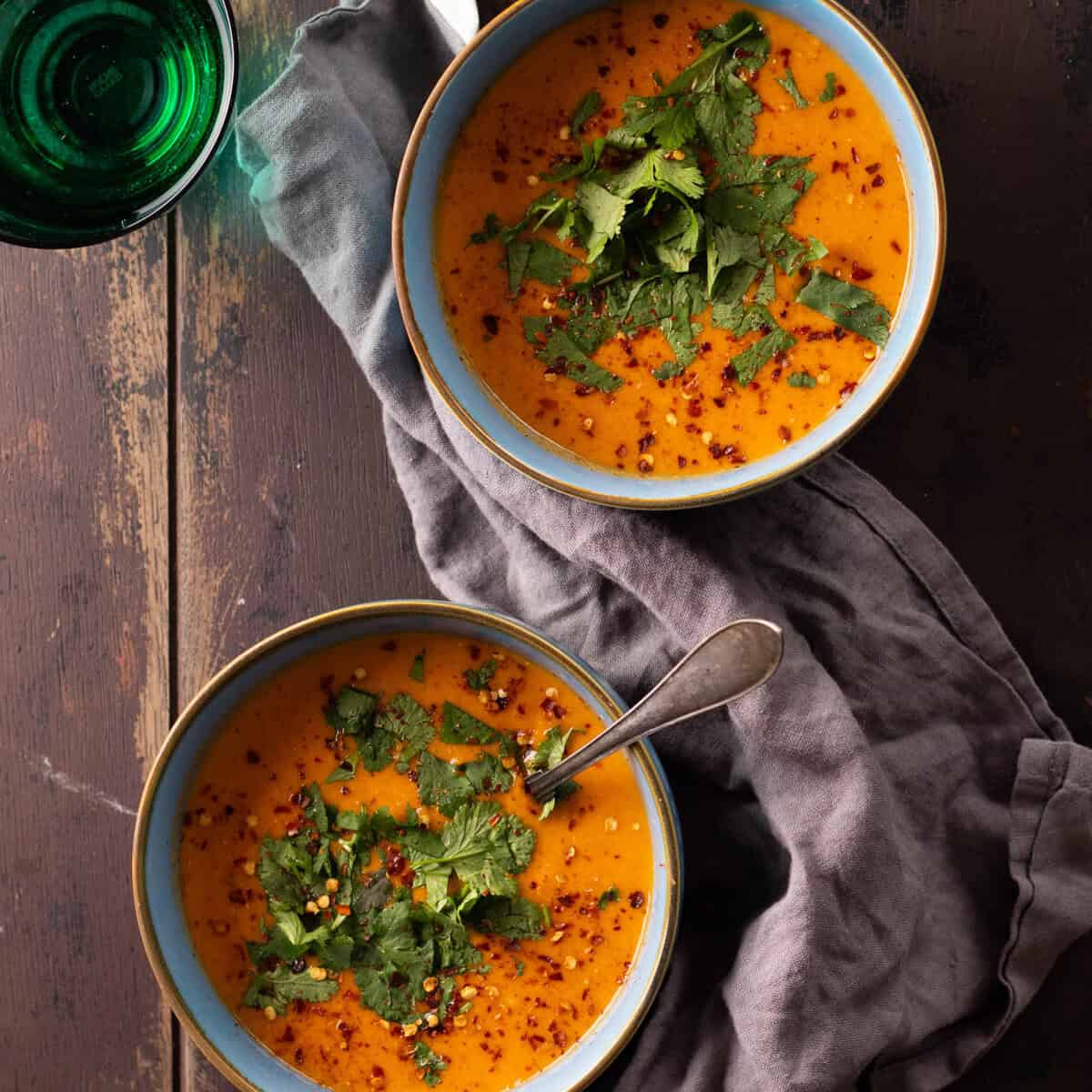 A blue bowl of creamy coconut lentil soup topped with chili flakes and cilantro.