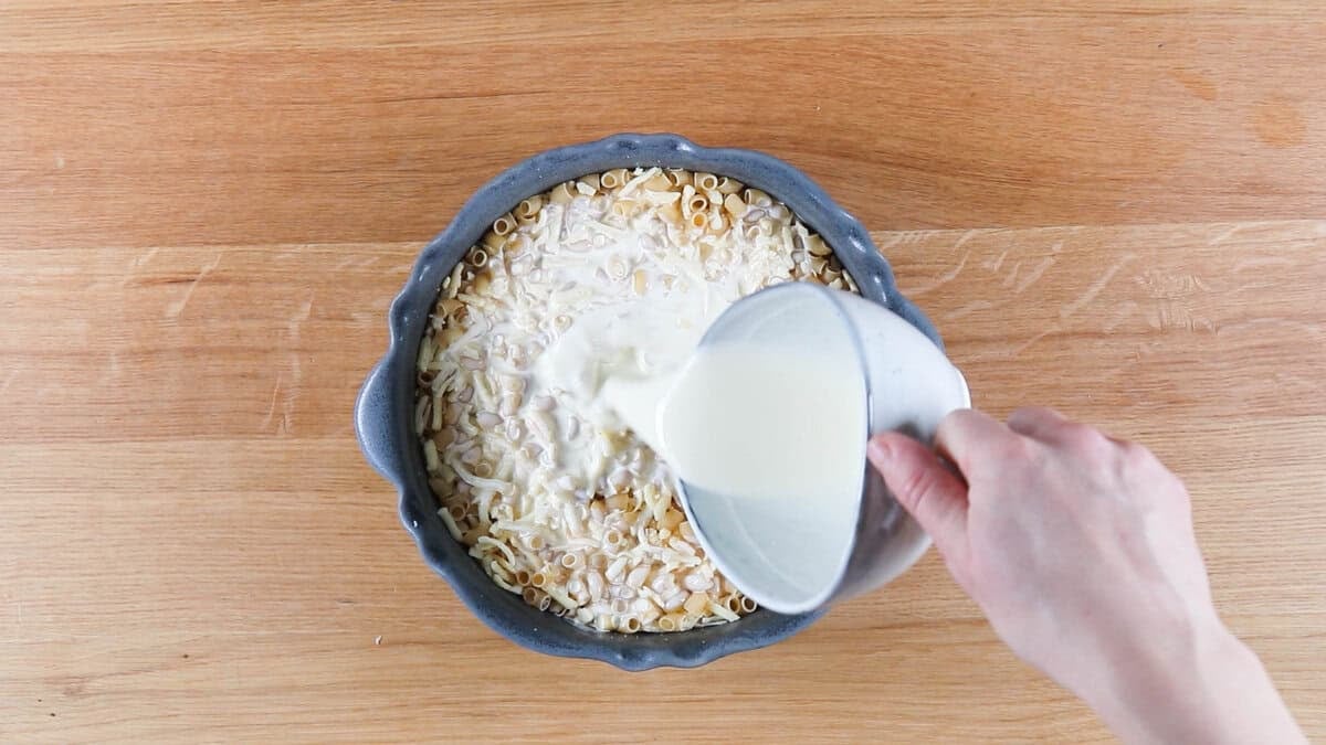 Pouring cream over macaroni and cheese to make 3 cheese mac and cheese.