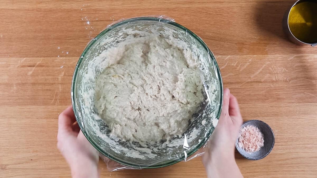 Focaccia dough after mixing together, covered with clingy plastic to proof.