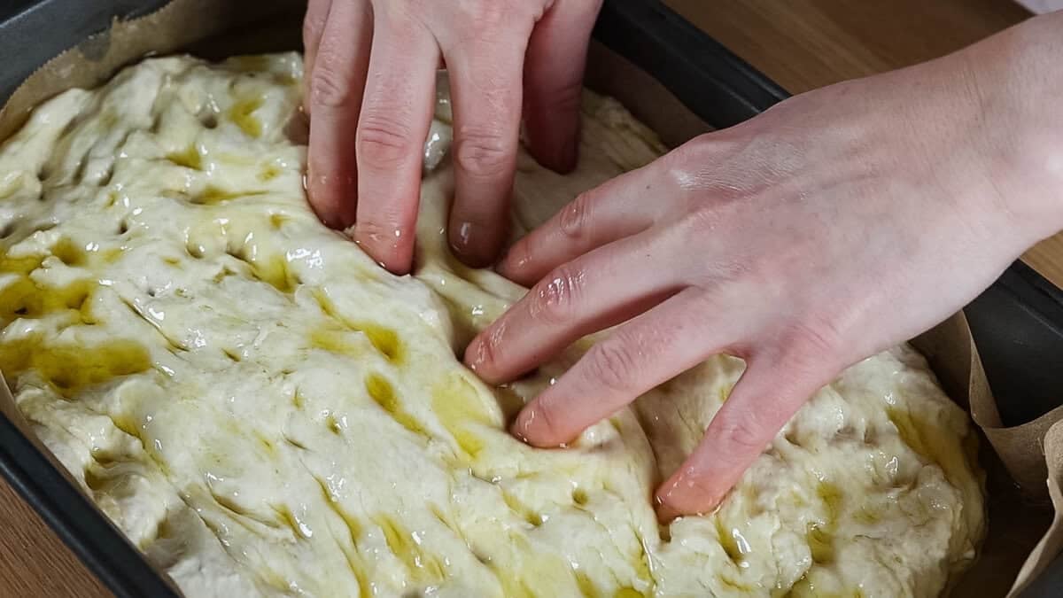 Using fingers to create indentations in focaccia dough.
