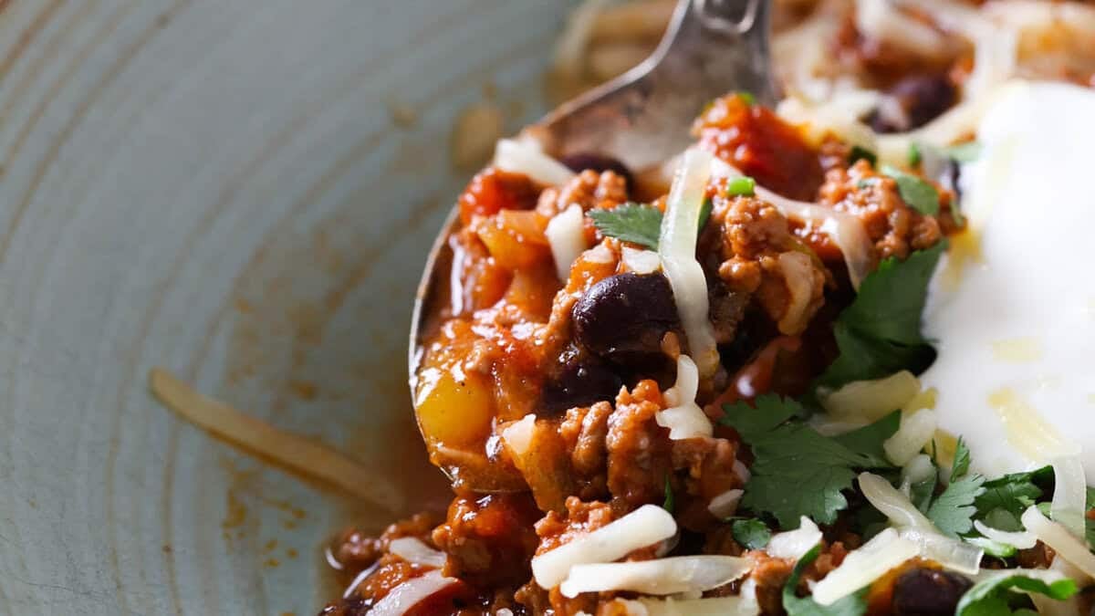 A green bowl with beef chili topped with sour cream, shredded cheese and fresh cilantro.