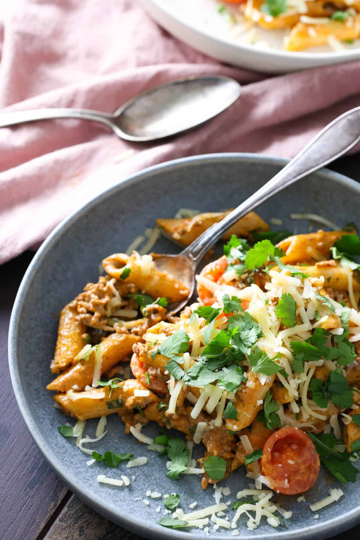 Taco pasta topped with shredded cheese and cilantro on a grey plate.