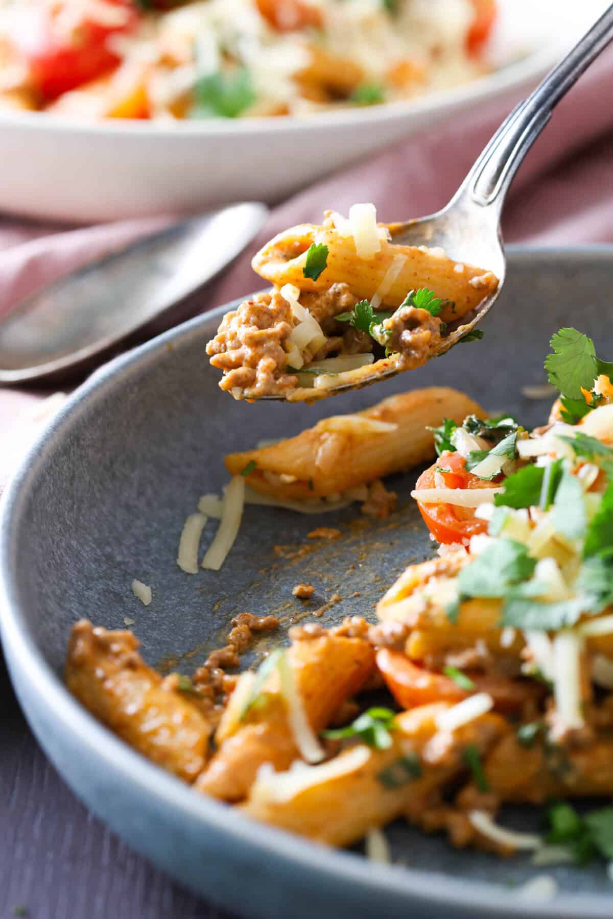 A spoonful of taco pasta being lifted off a blue plate.