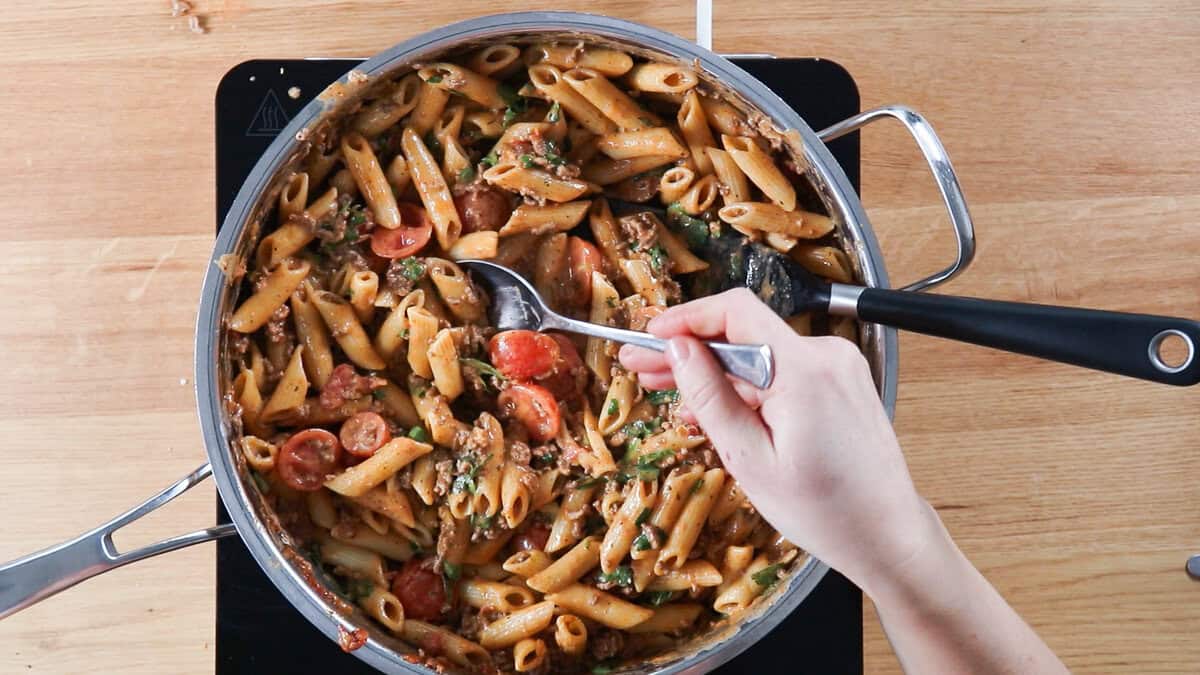 Taste testing taco pasta in a skillet.