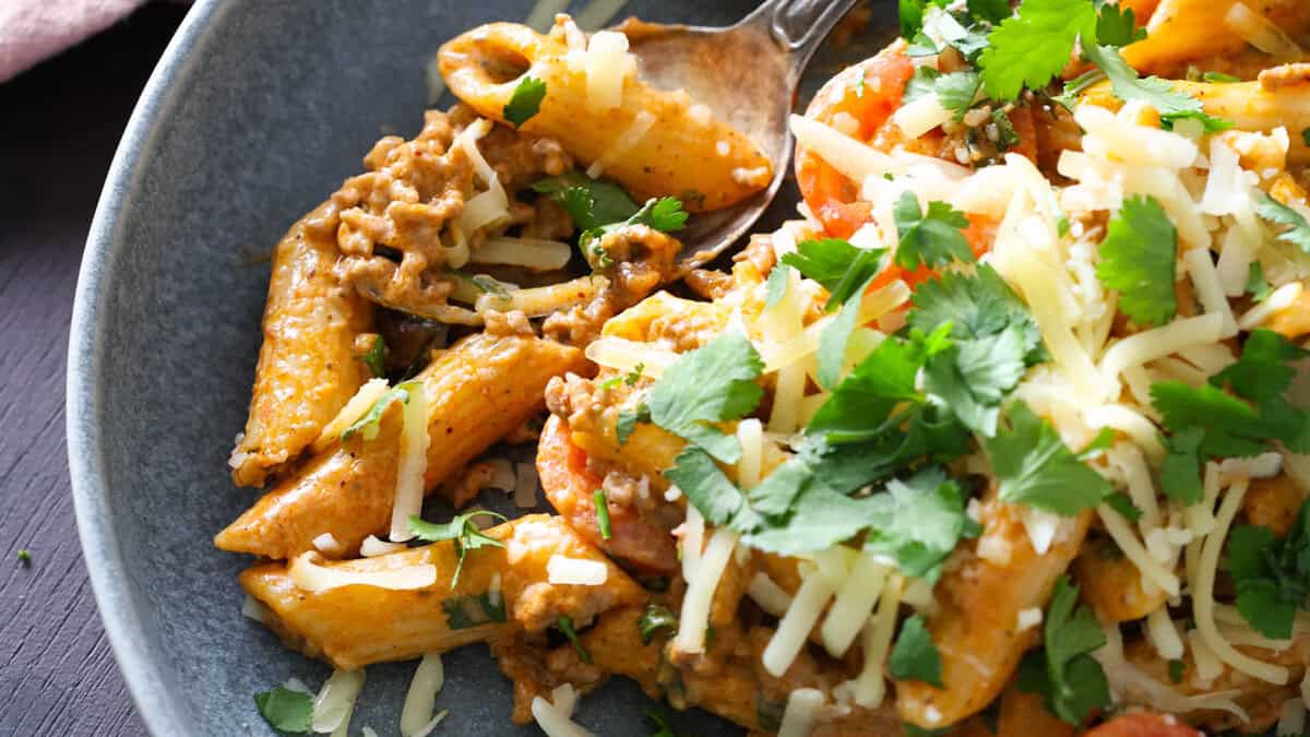 Taco pasta topped with shredded cheese and cilantro on a grey plate.