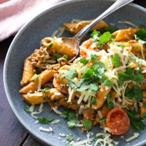 Taco pasta topped with shredded cheese and cilantro on a grey plate.