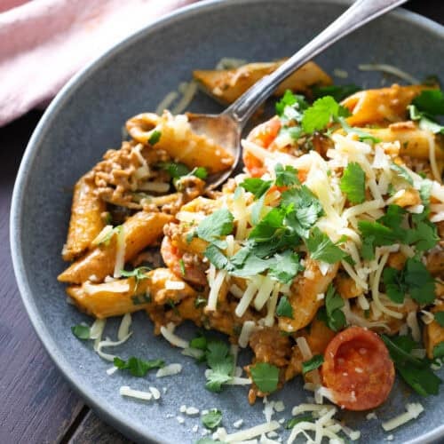 Taco pasta topped with shredded cheese and cilantro on a grey plate.