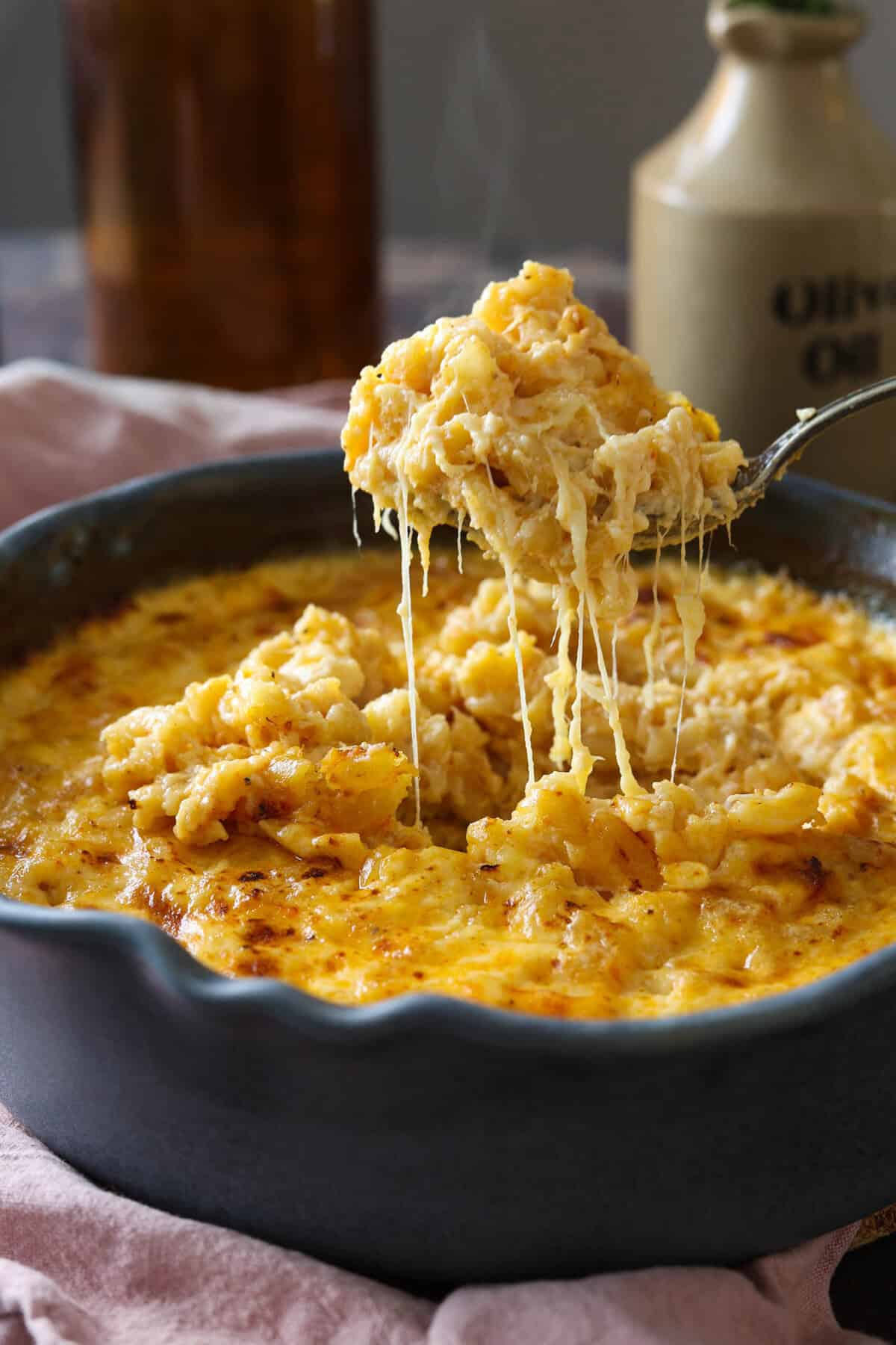 A spoonful of gouda mac and cheese being lifted out of the pan with a cheese pull.