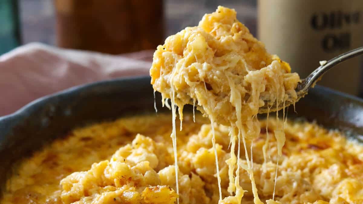 A spoonful of gouda mac and cheese being lifted out of the pan with a cheese pull.