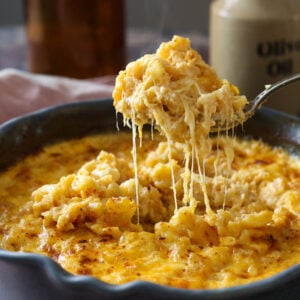A spoonful of gouda mac and cheese being lifted out of the pan with a cheese pull.