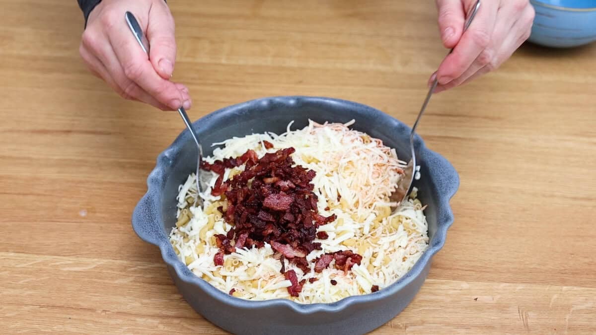 Mixing in bacon with macaroni and pasta to make bacon mac and cheese.