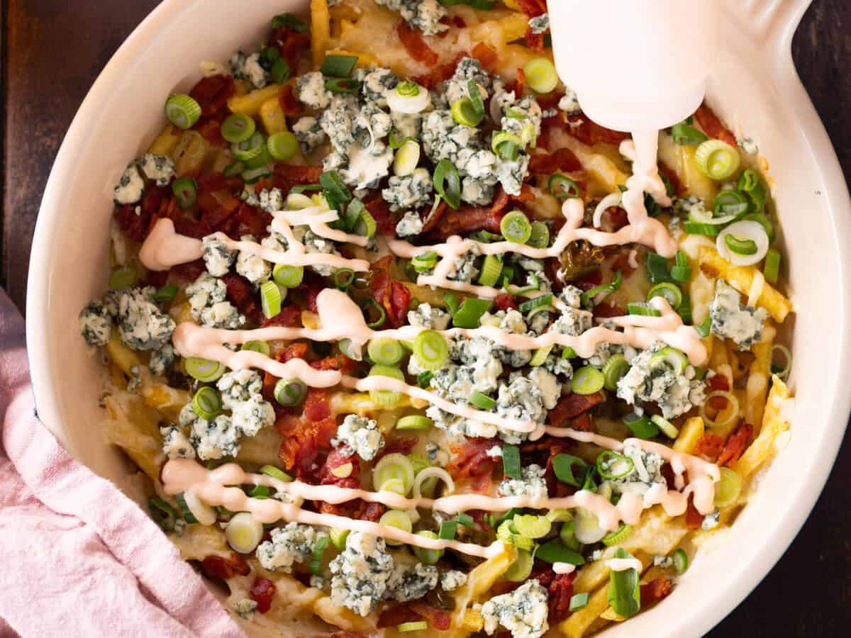 Drizzling buffalo fries with buffalo dipping sauce.