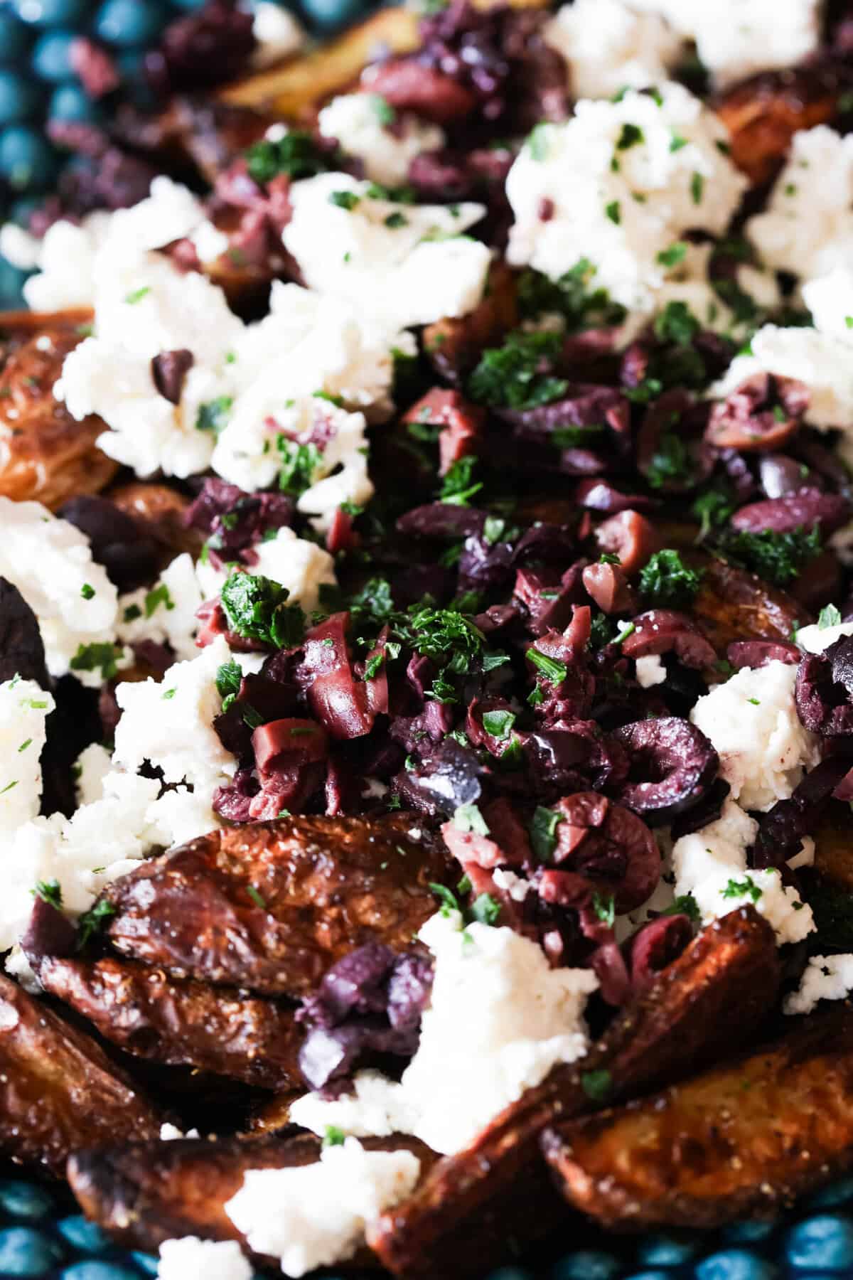 Close up of potato wedges topped with feta cheese and black olives.