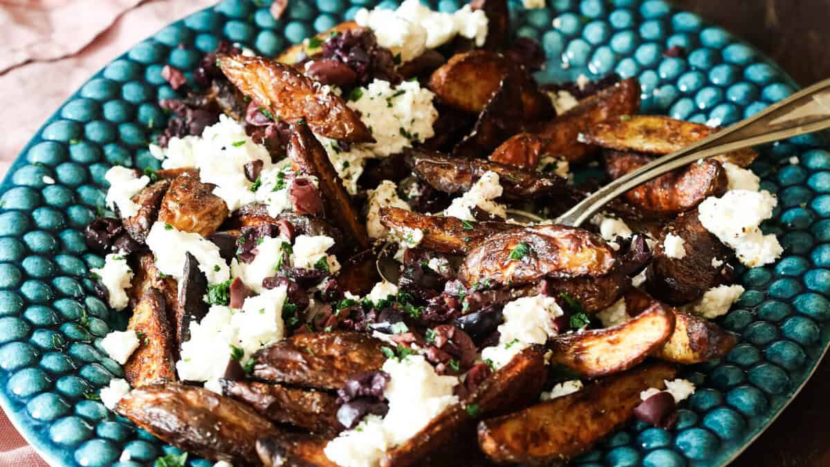 Potato wedges topped with feta cheese and chopped black olives on a blue plate.
