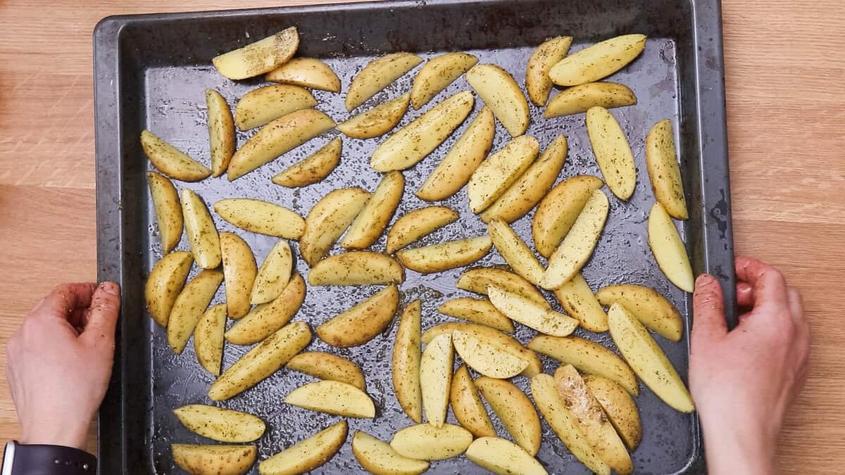 Seasoned potato wedges on a sheet pan before baking.