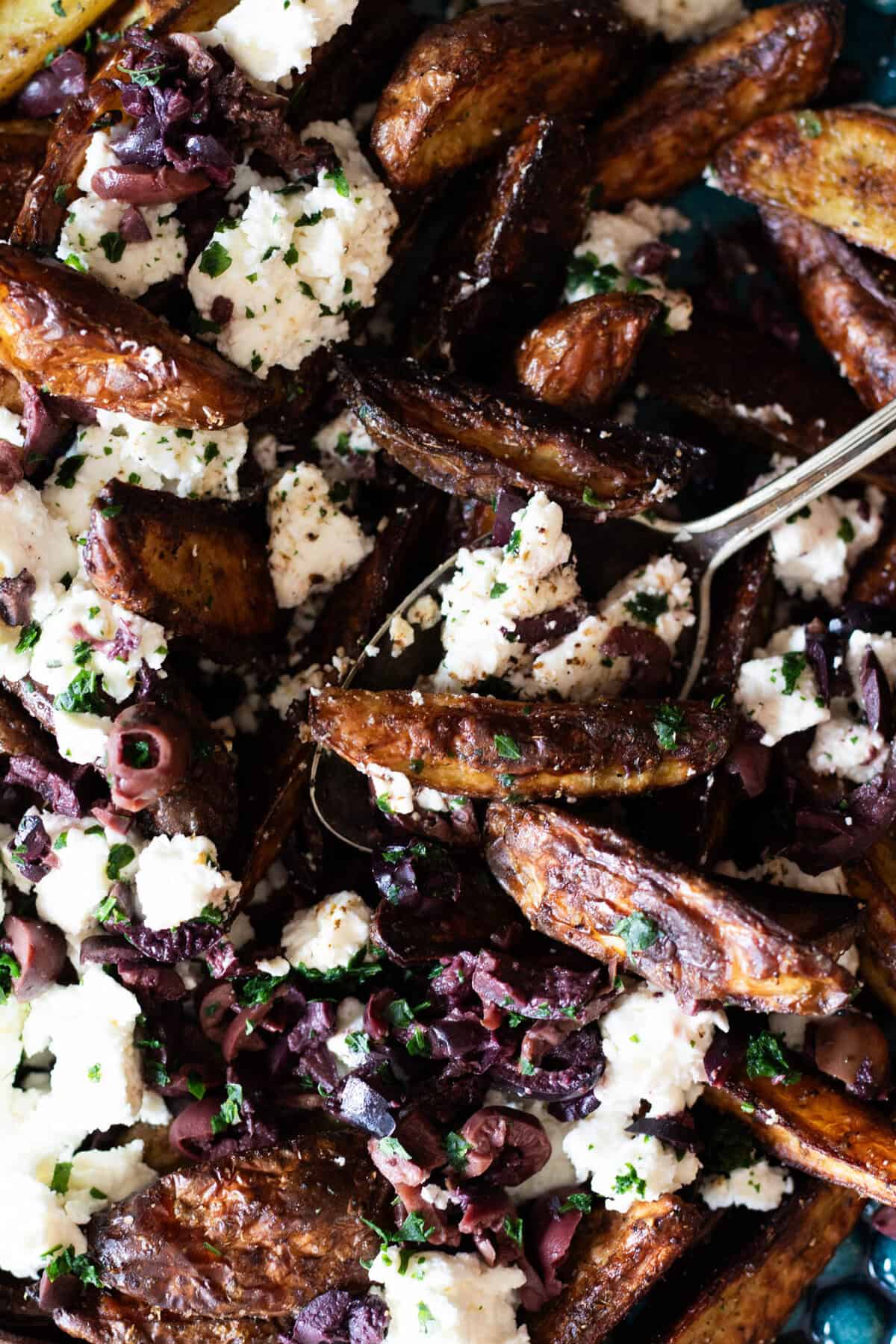 Potato wedges topped with feta cheese and chopped black olives on a blue plate.