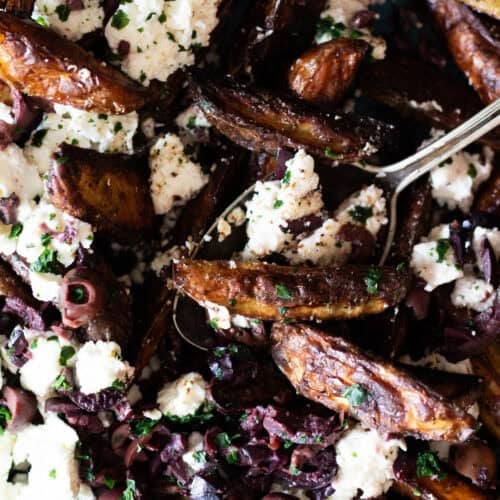 Close up of potato wedges topped with feta cheese and black olives.
