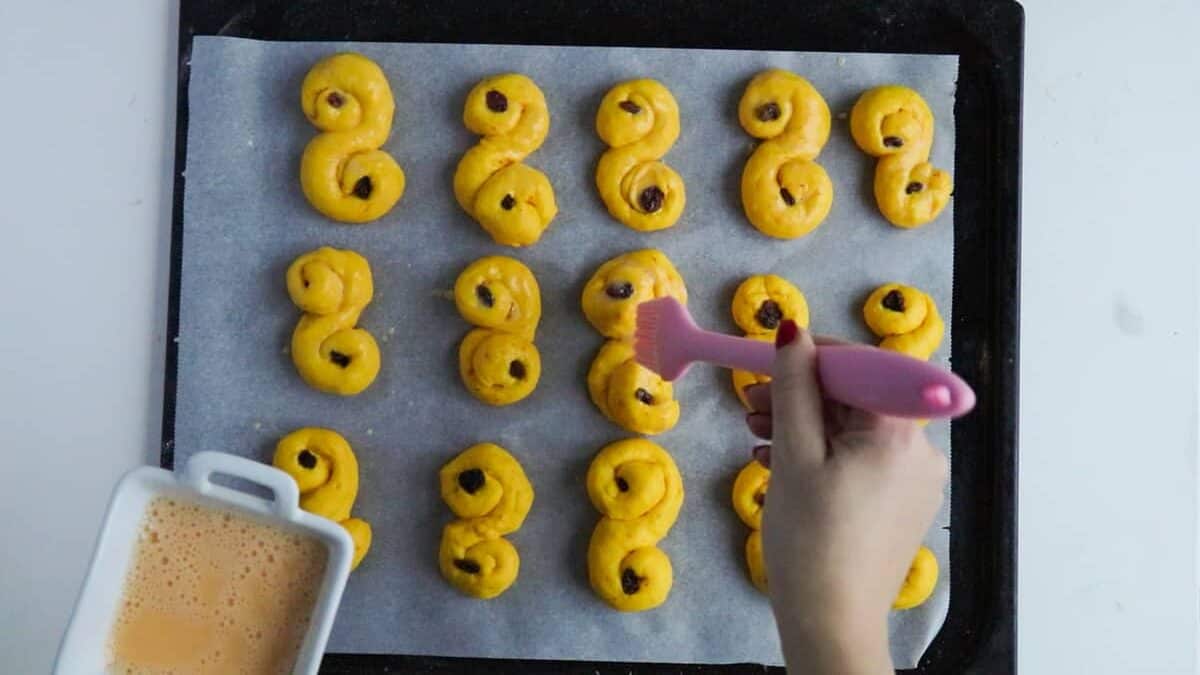 Brushing lussekatter with egg wash before baking.